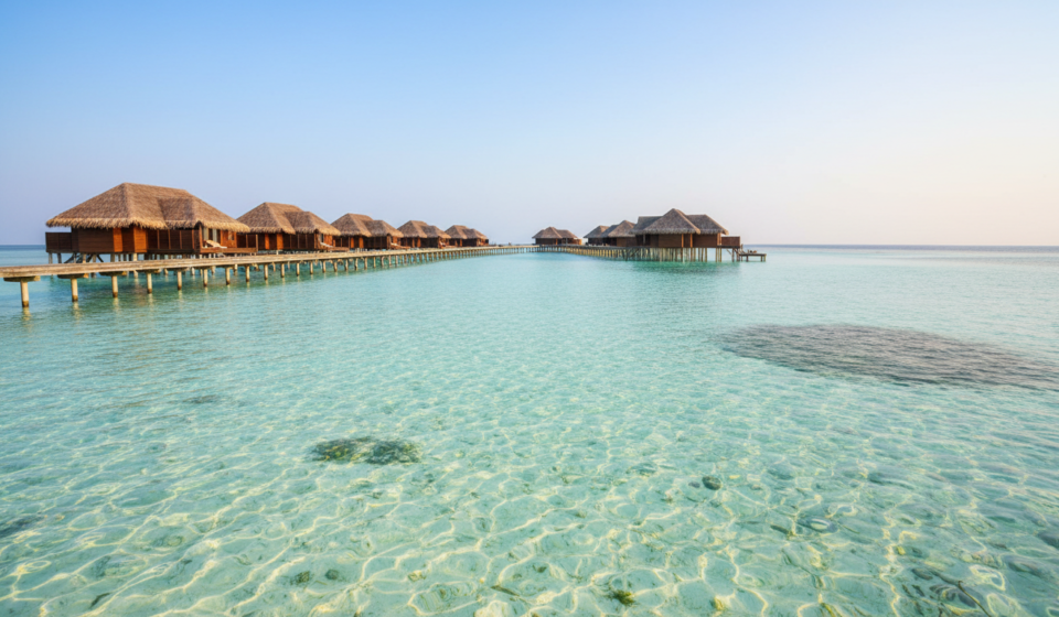 Best Time to Visit India and Maldives: Weather & Season Guide Calm turquoise lagoon and wooden overwater villa boardwalk in the Maldives under a bright blue sky.