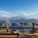 Sunlit mountain view of clear Himalayan peaks and colorful prayer flags under a bright autumn blue sky.