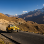 A yellow 4x4 vehicle driving along a winding asphalt mountain road in the high-altitude valley of Spiti.