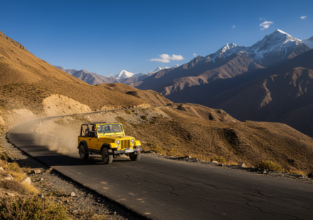 A yellow 4x4 vehicle driving along a winding asphalt mountain road in the high-altitude valley of Spiti.