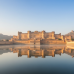 Amber Fort in Jaipur illuminated by warm morning sun, reflected in Maota Lake during clear autumn weather.