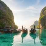 Longtail boats resting on clear turquoise water surrounded by dramatic green limestone cliffs in Thailand.