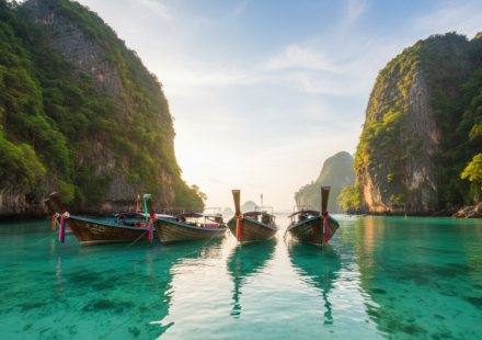 Longtail boats resting on clear turquoise water surrounded by dramatic green limestone cliffs in Thailand.
