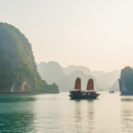 Traditional wooden junk boats sailing through misty emerald waters and limestone karsts in Ha Long Bay, Vietnam.
