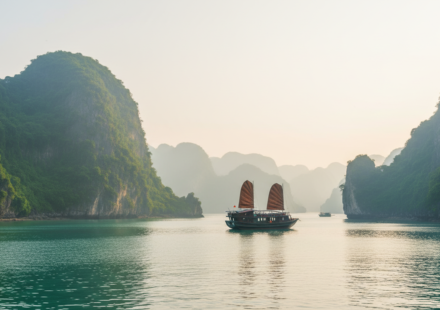 Traditional wooden junk boats sailing through misty emerald waters and limestone karsts in Ha Long Bay, Vietnam.