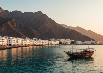 White Omani coastal buildings and mountains along Mutrah Corniche in Muscat under a clear golden hour sky.