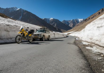 A paved Himalayan mountain road in Ladakh surrounded by melting snow walls and sharp barren rock peaks under a clear blue sky.