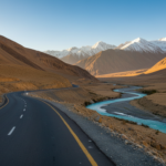 A paved mountain road winds through a broad Himalayan valley in North India under a clear morning sky.