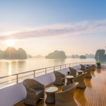 A white luxury cruise ship sailing between misty limestone karsts in the calm emerald waters of Ha Long Bay.