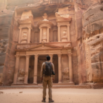 Traveler standing in the sandstone Siq canyon looking towards the ancient Treasury in Petra, Jordan.